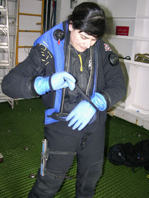 With the full blue-and-black drysuit completely on, Diane tapes on the third pair, waterproof blue gloves.