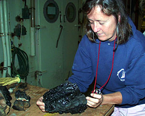 Geologist Susan Humphris uses a hand lens to look at a rock dredged from a young volcano. The rock’s glassy surface formed when the hot lava was rapidly quenched by cold seawater.  