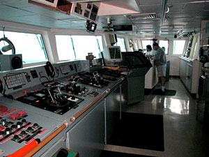 The bridge, with 3rd Mate Richard Bean and Able Seaman Jerry Graham on watch. The control panel is where the ship is steered and propelled. Today's weather was rough enough that the decks were closed. At such times, the bridge, which affords a view of the ocean in every direction, is the only place where you can see the water. It's also the only place where you can see the horizon, which comes in handy when combating seasickness.  