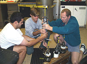Tim Rozan, Brian Glazer, and Martial Taillefert carefully remove the plastic cylinder containing the sediment core from its holder. They must try not to disturb the core and mix up the different layers. 