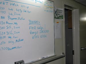 The night�s event�finding the first salps�is commemorated on the whiteboard, the team�s message center, noting the net (Bongo 2), the time (0030, or 30 minutes past midnight), and the latitude and longitude of the bongo tow. On the left is a list of which researchers are working which hours. 