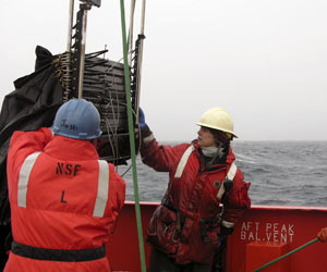 During a daytime plankton tow, L. M. Gould Marine Technician Jamee Johnson and WHOI engineering assistant Josh Eaton (blue hard hat) stabilize MOCNESS as the winch lifts it over the stern.