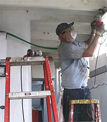 Bosun Bill Kamholtz grinds rust from the overheads on the 01 deck level.