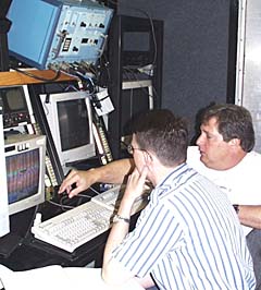 Steve Gegg (right) explains the vehicle navigation system to Dan Scheirer in the Control Van. The blue electronics box above them is used to “talk” to the transponders on the seafloor; they “reply” and tell us where the sonar “fish” is located.