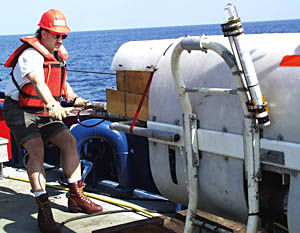 Craig Elder, a member of Woods Hole Oceanographic Institution’s Deep Submergence Operations Group, holds the tailend of the sonar fish. Because of its shape, this part is called the “lollipop.” You can see that Craig is wearing a hard hat and work vest. Safety is an important concern, especially when moving heavy equipment on a rolling platform like a ship on the ocean. 
