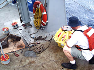 Today, right after breakfast, we started setting transponders at the bottom of the ocean so that we can navigate the DSL-120 sonar fish in our survey area near 3° 20’N on the East Pacific Rise crest . Randy Dickau is kneeling by the transponder; the yellow ball in the right side of the photo. Notice that he is wearing a working life-vest (or work vest) that will help keep him afloat if he falls in the water. Everyone putting instruments over the side of the ship must wear one. The thin wire is the tether line that attaches the transponder to the steel plates on the left side of the photo. The steel plates are the anchor that keeps the transponder at the bottom of the ocean. When we want to get the transponder back, we send a sound signal down to it, and it releases from the anchor and floats back up to the surface. Check out the information on transponders in the “Navigation” section of “Oceanographic Tools” located in the “About the Cruise” part of the web site. 