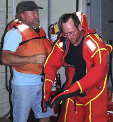Ron Comer (left) shows Randy Dickau how to put 
              on a survival suit, usually called a Gumby suit because you 
              look like the cartoon character when you put it on.