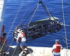Argo II is lowered over the stern of R/V Melville for the first time on this expedition. Even though the weather is terrific and the seas are calm, we are still on a ship that rolls gently. Argo II weighs over 6000 pounds and so it has to be very carefully controlled when it is lifted off the deck so that it does not start swinging and cause damage. To do this, several people tend “safety lines” that are attached to the frame of Argo II to keep it steady. In this photo, Argo II is safely lowered over the side, and Rob Palomares (left) and Ron Comer continue to tend their safety lines while Randy Dickau is removing another of the safety lines . 