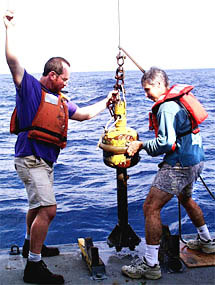 Randy Dickau (left), one of Scripp’s Resident Technicians, and Dan Fornari (right) steady the rock corer for a deployment. Randy is giving instructions with hand signals to the person operating the winch. We have started using the rock corer to take small samples of volcanic glass from the lava pillows. It weighs about 400 pounds and has seven cutters on the end. We send the corer down on a wire and crash it into the seafloor lava flows. The glass that chips off the lava gets stuck in the surfboard wax that fills the cutters.