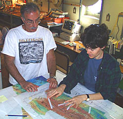 Mike Perfit and Maya Tolstoy plan the DSL-120 sonar survey for the 1°45’N study site. They are placing long white strips of paper that represent the 1000 meter width of each survey line on the multibeam bathymetry map. This helps them determine how much seafloor the DSL-120 sonar will “see” along each line.