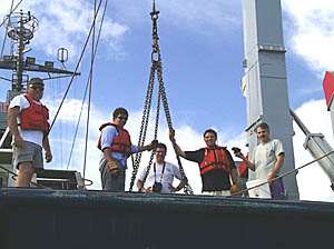 Today’s dredging crew on the fantail of R/V Melville. From left to right are Ron Comer, Jon Burgess, Dan Scheirer (framed in the dredge chain), Ben Wigham, and Dan Fornari holding one of the samples recovered in the dredge.