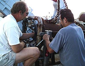 Bob “Yogi” Elder (left) and Rob Palomares install the 12 kiloHertz pinger (the silver cylinder) on the DSL-120 clump weight. The clump weight is placed above the DSL-120 so that it absorbs most of the movement of the ship. This allows the sonar fish to “fly” in a straight line rather than going up and down with the ship. The clump weight is about 30 meters in front of the sonar fish. The pinger tells how far above the seafloor the clump weight is. If the distance between the seafloor and the clump weight decreases, then we know that the seafloor is getting shallower and we have to pull the sonar fish up. It the distance between the seafloor and the clump weight increases, then the seafloor is getting deeper and we can lower the sonar fish.