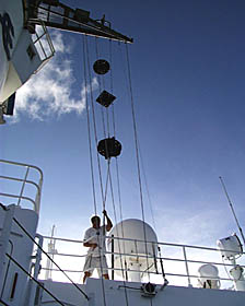 Dave Murline hoists the “Day Shapes”. The shapes and sequence of “ball, diamond, ball” are hoisted when we are towing equipment at slow speeds and cannot maneuver very well. It signals to nearby ships that we have a “restriction in ability to maneuver”. When any vessel is displaying these shapes, nearby ships stay well away from it and give it the right of way. At night, the shapes are replaced by a “red, white, red” sequence of lights that means the same. One of the satellite antennas domes is behind Dave. 