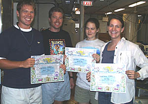 Captain Eric Buck (2nd from left) hands out Equator Crossing Certificates to new Shellbacks Ben Wigham (left), Kate Gans (next to Capt. Buck), and Julia Getsiv.