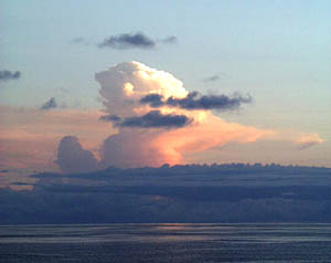 A large storm cloud towers over the lower cloud layers at sunset. 