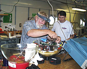 Tom Crook (left) repairs one of the transponders as Jeff Keeler stands by to assist. Tom is preparing the transponders for the next cruise.