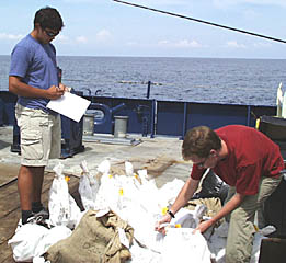 Jon Burgess (left) and Peter Lean sort through some of the many bags of dredged rocks collected on the cruise. Once they have made a list of them, the bags will be loaded into containers to be shipped to the University of Florida and Woods Hole Oceanographic Institution.