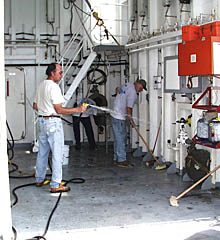James Eubanks (left), Bill Kamholtz (the Bosun), and Cletus Finnell (background) clean the forward storage hanger on the starboard side of R/V Melville in preparation for the next cruise. The laboratory areas on the ship will be cleaned by the science team so that they are ready for the next group of scientists to come on board and set up their equipment.