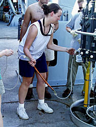 Julia draws a sample from one of the Niskin bottles on the CTD rosette sampling system. The white rubber tubing is attached to the white nozzle on the bottom of bottle, and the sample is collected in the copper tube that Julia is holding. Great care has to be taken so that there is no contamination either between samples from different bottles or anything that is on their hands or on the ship. 