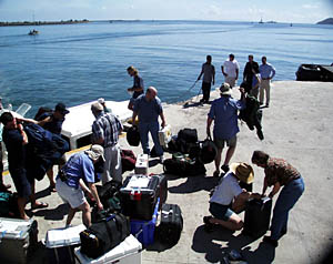 Researchers wait on the dock in the Seychelles capital Victoria for a ride to the WHOI research vessel Knorr. Chocolate bars, microscopes and clothes are some of the items squeezed into dozens of bags. In three days they will pick up another 70-tons of pre-shipped supplies during a stop at Mauritius, an island located 950 miles south of the Seychelles.  