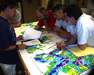 Using rainbow-colored bathymetric charts, researchers Bob Collier, Dan Fornari, Marvin Lilley and Susan Humphris plan explorations to different research areas. The bathymetric charts measure water depth -- the distance from the sea surface to the bottom of the ocean. Reds, oranges and yellows indicate shallow areas, while greens, blues and purples mark deeper spots.  