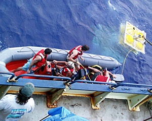 Crew members in the work boat pull alongside Knorr with the elevator in tow.  