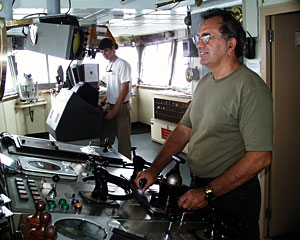 Seaman Ed Graham stands at the ship’s control panel on the bridge, while Third Mate Adam Seamans checks the radar for other ships and rain squalls.  