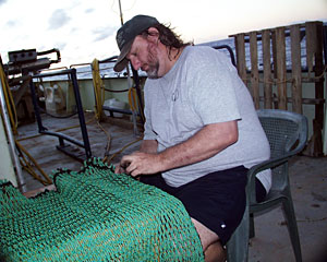 Shipboard Technician Dave Sims sews netting that will line the rock dredge.  