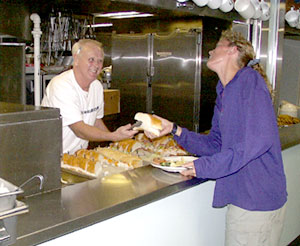 Ed Miller, Senior Cook, serves a lunch of sub sandwiches to Karen Harpp.  