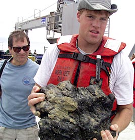  Mark Kurz looks on as Rob Otto carries the final rock from the last dredge of the cruise. 