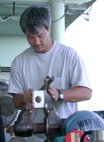 Able Bodied Seaman Patrick Hennessy shaves a Styrofoam block that will be placed beneath the CTD and rosette water sampler to help slide it across the deck. 