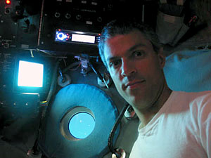 Dive and Discover writer Joe Appel, inside Alvin and about 1350 meters beneath the ocean surface. Joe was the starboard observer, so his primary task was recording which samples were collected and where. In the center of the photograph is the starboard window; at left is the starboard video monitor, which can show images from various cameras attached to the sub; up by Joe's head is the all-important CD player. 