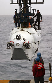  Despite misting rain and cold wind, eager observers collect on deck at 7:30 a.m. to watch the first Alvin dive of the expedition. Two swimmers standing on the sub—Mark Spear (right) and Raul Martinez—are certified to help deploy Alvin after it is lowered into the water.