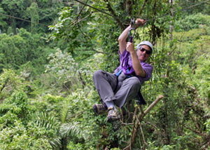 WHOI geologist Dan Fornari races from tree to tree on a zip line, a wire extending through an area of the Costa Rican jungle near Arenal Volcano. He uses a gloved hand to steady his body, and the same hand to pull on the wire to slow down. 