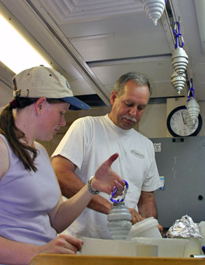 Biologist Rhian Waller and chemist Dan Stuermer dip weights into wax to make them sticky. On command, TowCam will drop the weights to the seafloor to collect shards of glassy lava. On shore scientists will analyze the shards for their chemical composition. (Photo by Amy Nevala)