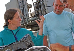 Geochemist Susan Humphris shows Dan Stuermer and Vinod Khosla a rock sample collected by Alvin. The thin, black, glassy surface forms when lava erupts on the seafloor. (Photo by Amy Nevala)