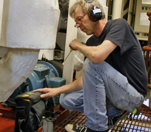 Chief engineer Jeff Little, wearing ear protection in the ship’s noisy engine room, checks the vibration level on a pump and motor used for the air conditioning system.