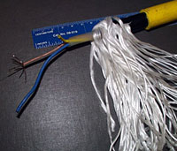 A piece of fiber optic cable unraveled to show the three colored wires containing the glass fibers. The fuzzy white material is the Spectra.